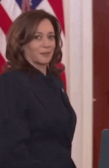 a woman in a suit is standing in front of an american flag and smiling .