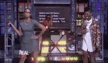 two women are dancing in front of a screen that says the real on it