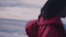 a woman in a red jacket is walking along the beach .