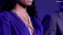 a woman wearing a purple dress and a diamond necklace is smiling
