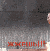 a man in a black tank top is standing in front of a wall with the words " жжешь " written in red letters