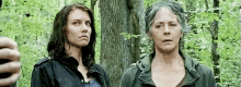 two women standing next to each other in the woods .