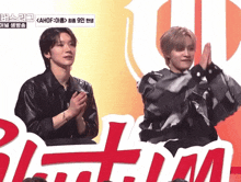 two men applauding in front of a sign that says ' bloom '