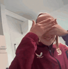 a woman covering her eyes with her hands and wearing a jacket that says castore on it