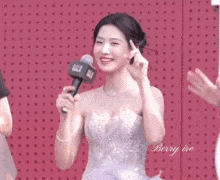 a woman in a wedding dress is holding a microphone and smiling .