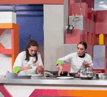 two women are standing at a counter in a kitchen cooking food .
