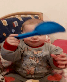 a baby wearing a shirt with a cat on it is holding a blue spoon in front of his face