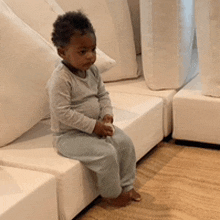 a baby is sitting on a white couch looking at something