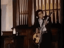 a man in a suit and tie is playing a guitar in front of an organ .