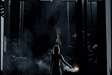 a woman is holding a glowing object in a dark forest with a green face on her head .