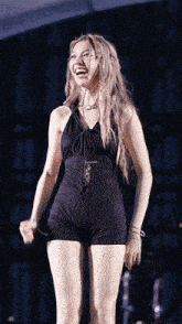 a woman wearing a black jumpsuit is laughing and holding a microphone