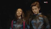 a boy and a girl are standing next to each other with a trt logo in the background