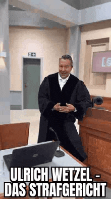 a man in a judge 's robe is standing in a courtroom in front of a laptop .
