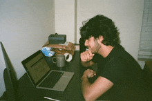 a man sits at a desk with a laptop and a mug on it