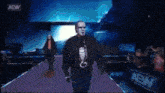 a man in a mask walks down a purple carpet in front of a aew banner