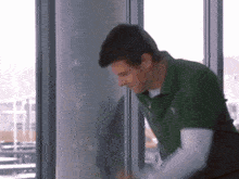 a man in a green shirt is leaning against a window