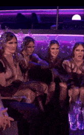 a group of women are sitting in a dark room with purple lights
