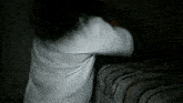 a woman in a white shirt is standing next to a bed in the dark .