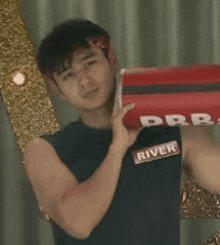 a man wearing a river tank top holds a red box in his hand