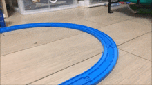 a toy train going around a blue track on a wooden floor