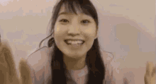 a close up of a woman in a pink shirt smiling and waving her hands .