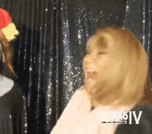 a woman laughs in front of a black curtain with reina6iv written on the bottom