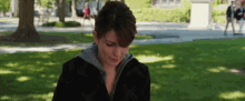a woman in a black jacket is standing in a park looking down .