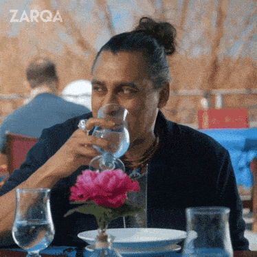 a man sits at a table drinking a glass of water with the word zarqa behind him