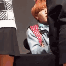 a person with red hair and glasses is sitting on a chair with their legs crossed .