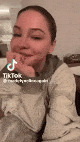 a woman is sitting at a table with her hand on her chin and a tik tok sticker on her face .