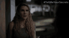 a woman stands in front of a sign that says # tellmeyoursecrets