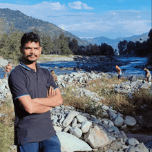 a man with his arms crossed is standing in front of a river