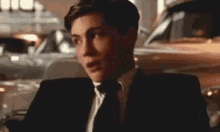 a man in a suit and tie is standing next to a car