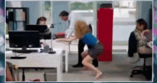 a woman in a blue shirt is running barefoot in an office while a man stands behind her