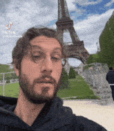 a man with glasses and a beard is standing in front of the eiffel tower in paris