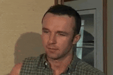 a man in a plaid shirt is standing in front of a door and looking at the camera .