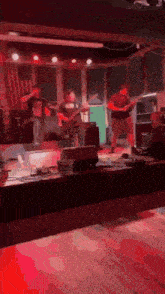 a group of men are playing guitars on a stage in a dark room .