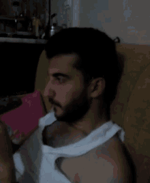 a man with a beard wearing a white tank top sits on a chair