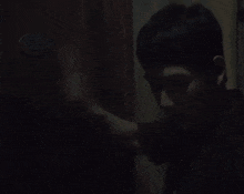 a man in a black shirt is standing in the dark looking at a door .