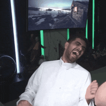 a man in a white shirt is laughing in front of a tv screen