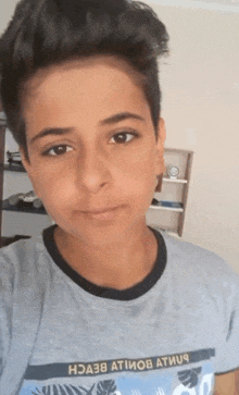 a young boy taking a selfie wearing a t-shirt that says " hoa38 atiwob atiuq "