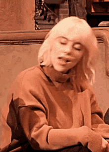 billie eilish is sitting on a couch with her eyes closed and a sweater on .