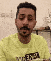 a man with a beard and mustache is wearing a yellow t-shirt that says ' ikat ' on it .