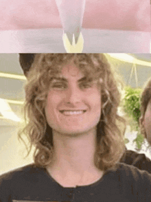 a man with long curly hair is smiling in a black shirt