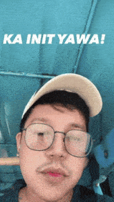a man wearing glasses and a baseball cap says ka init yawa