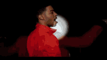 a close up of a man 's face in a dark room with a red shirt on .