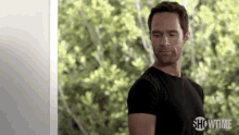 a man in a black shirt is standing in front of a window and trees .