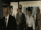 a man in a suit and tie is walking with a group of people in uniforms .