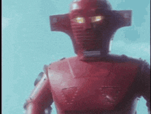 a red robot is standing in front of a blue sky with its eyes glowing .