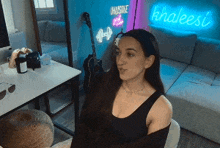 a woman sitting in front of a khaleesi neon sign